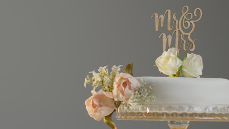 Close-Up-Of-Wedding-Cake-On-Stand-Against-Grey-Studio-Background-At-Wedding-Reception